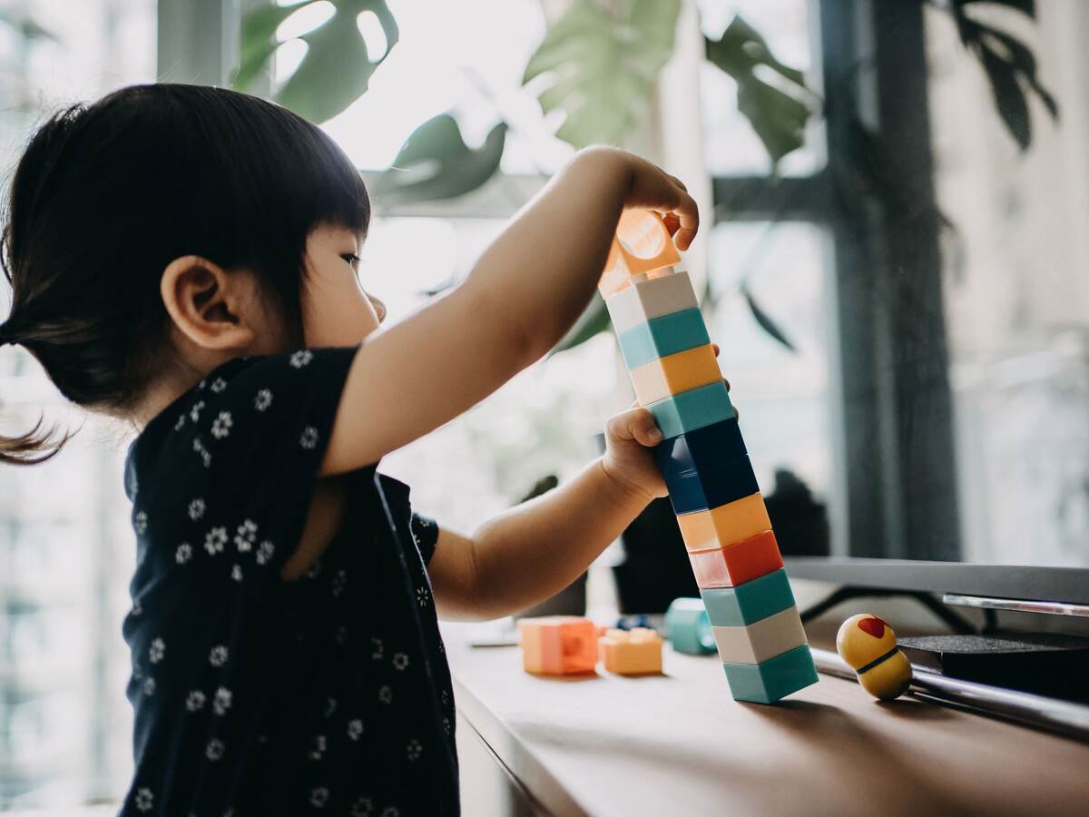 Creative little toddler girl playing with colorful building blocks at home.